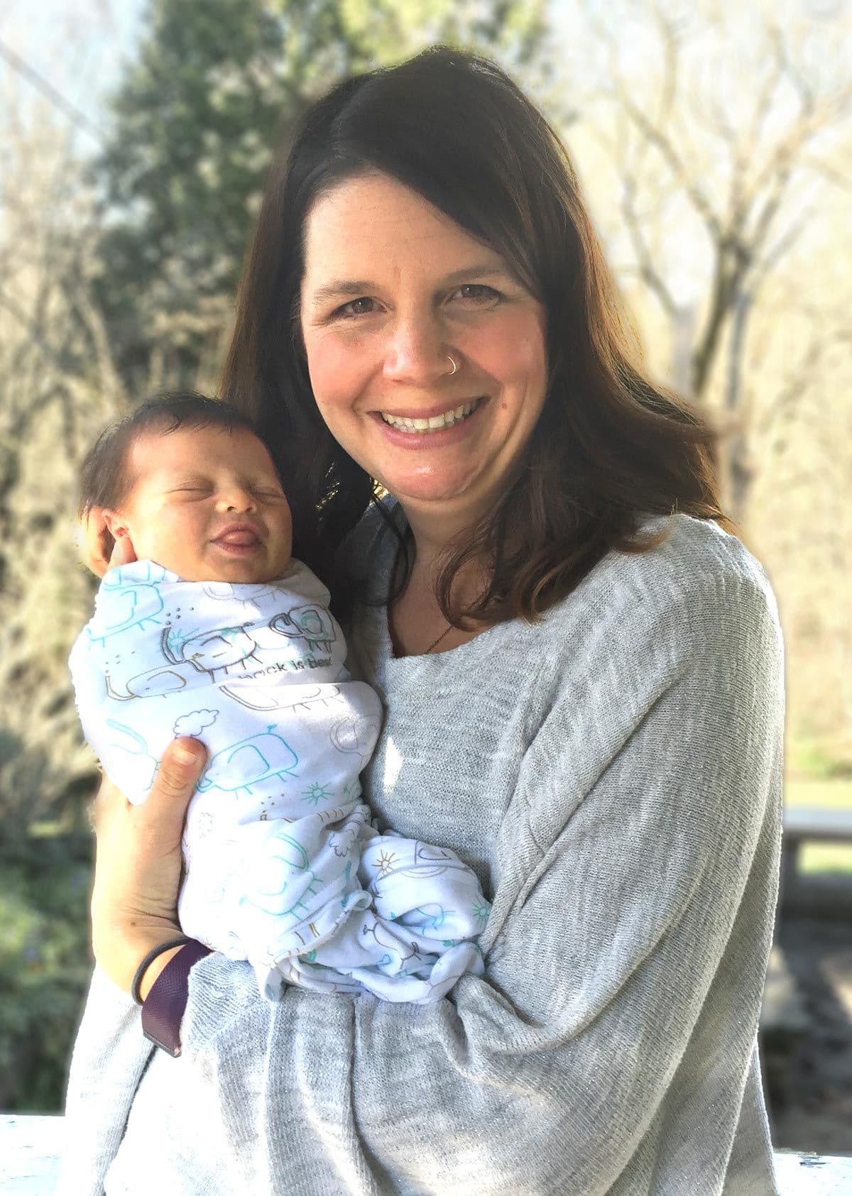 Jen Laird smiling while holding a newborn outdoors